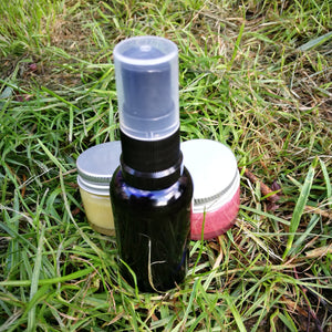 blue spray bottle on grass in front of 2 lip balm jars